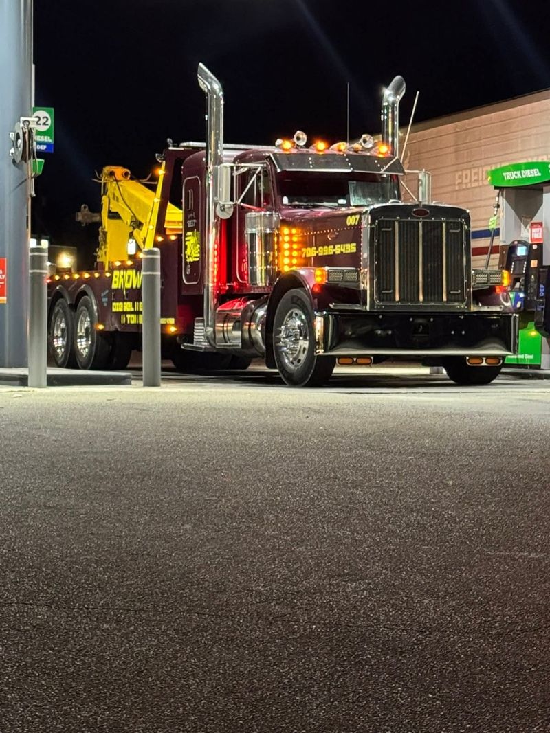 Brown's burgundy and yellow wrecker parked beside diesel pumps at night.