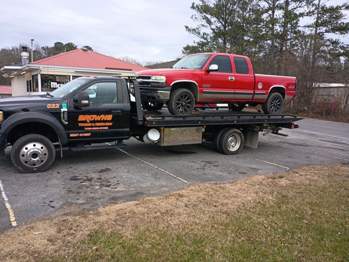 Brown's rollback carrying a red pickup truck on its deck.