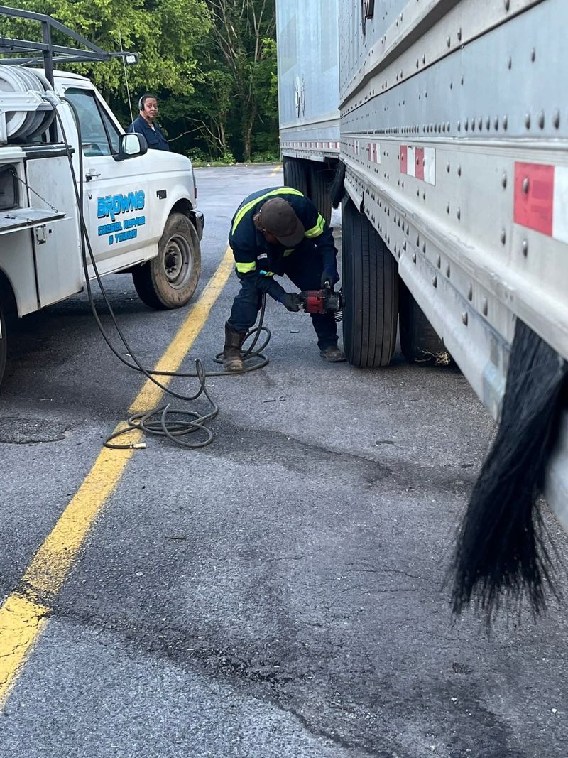 A technician working at a trailer wheel beside a Brown's service truck.