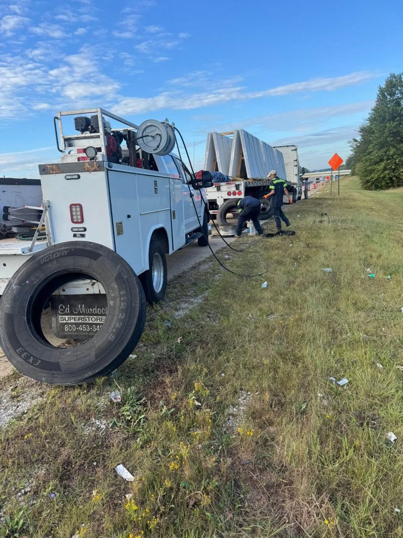 A service truck and technicians working with tires beside a flatbed trailer on a highway shoulder.